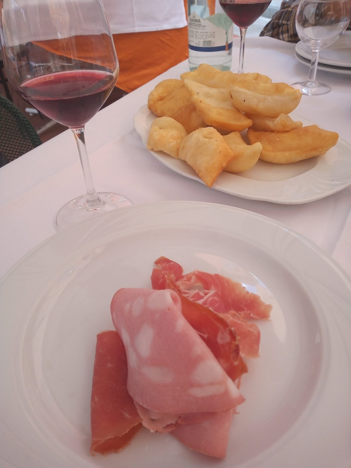 Gnocco fritto dorato servito con affettati e un calice di lambrusco.