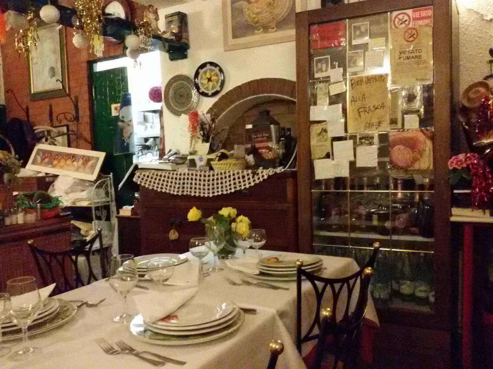 La piccola sala dell'Hostaria La Frasca: pareti coperte di fotografie e quadri, tavoli apparecchiati con fiori gialli.